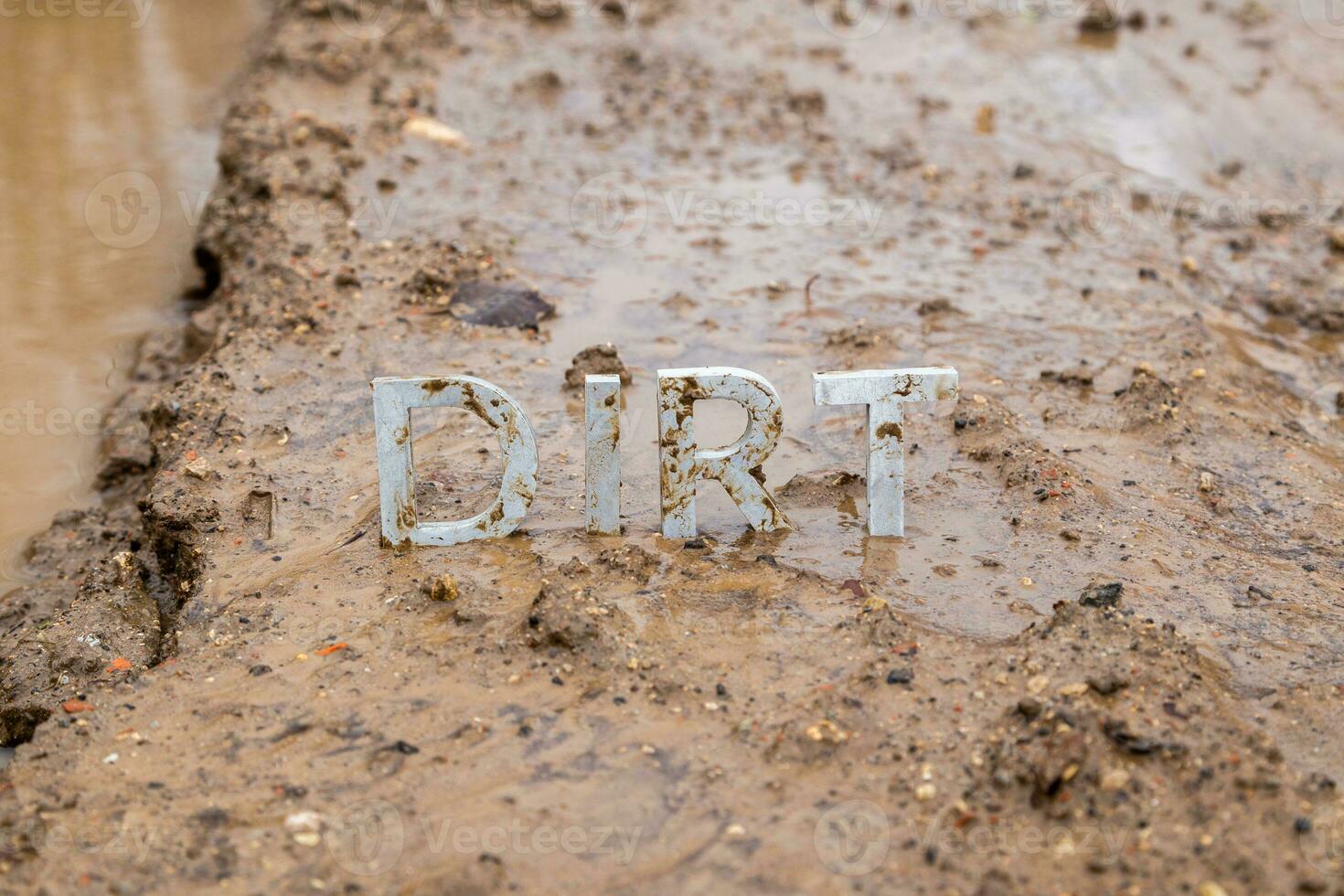 a palavra sujeira composta de letras de metal prateado na superfície de argila molhada foto