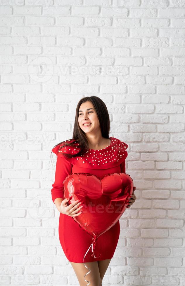 jovem morena de vestido vermelho segurando um balão de coração vermelho foto