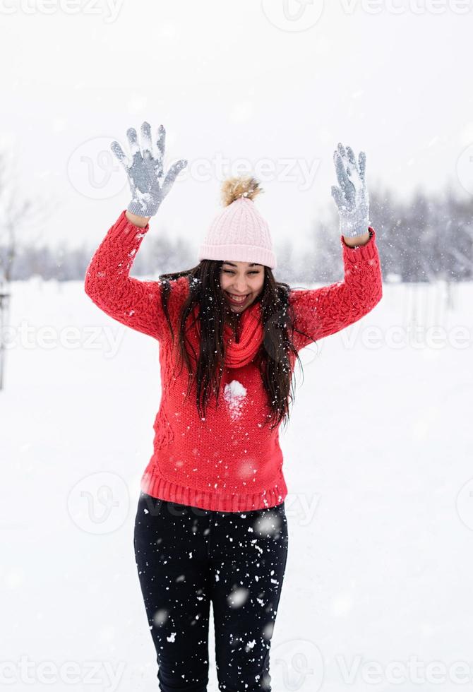 jovem morena de suéter vermelho brincando com a neve no parque foto