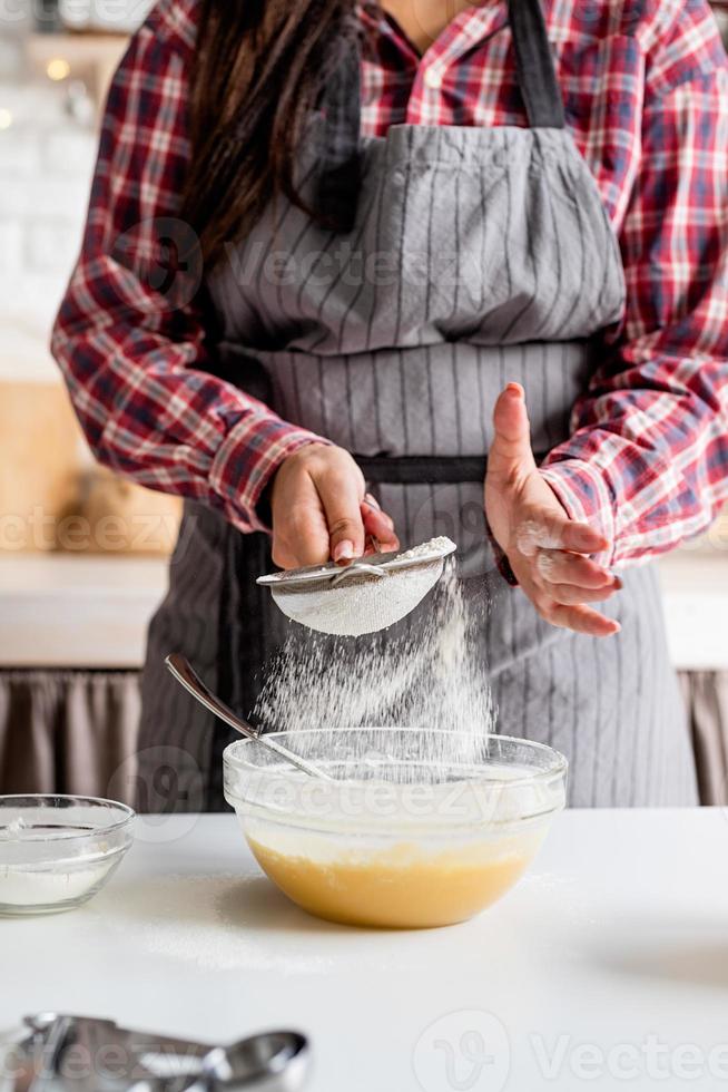 jovem latina servindo farinha na massa e cozinhando na cozinha foto