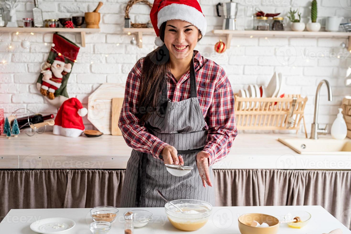 jovem latina servindo farinha na massa e cozinhando na cozinha foto