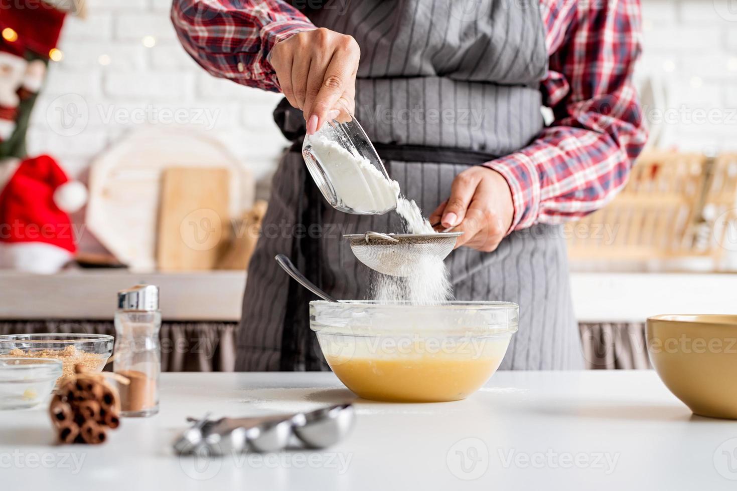 jovem latina servindo farinha na massa e cozinhando na cozinha foto