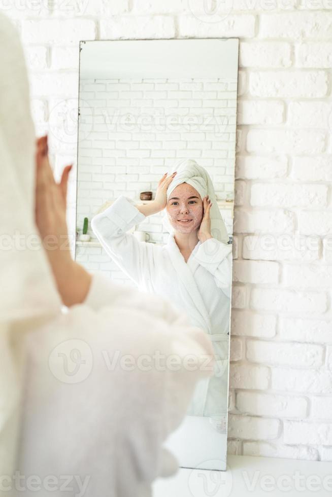 jovem feliz aplicando esfoliante facial no rosto foto