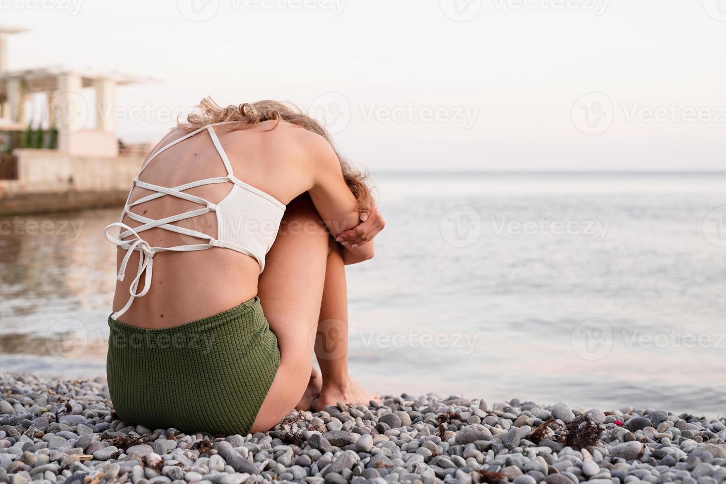 jovem mulher deprimida sentada na praia, vista traseira foto