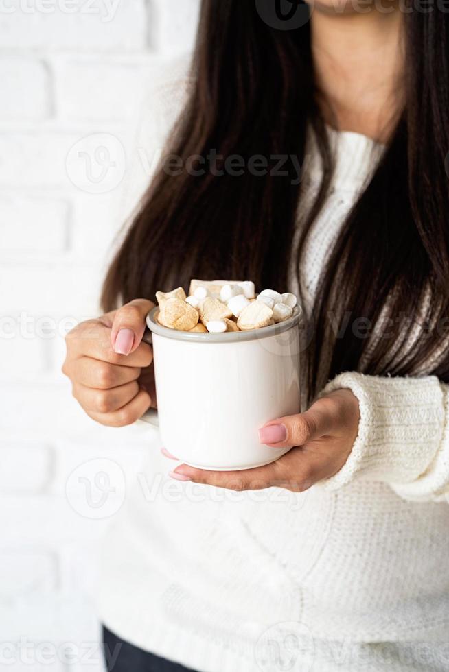 mulher morena segurando uma xícara de chocolate com marshmallow foto