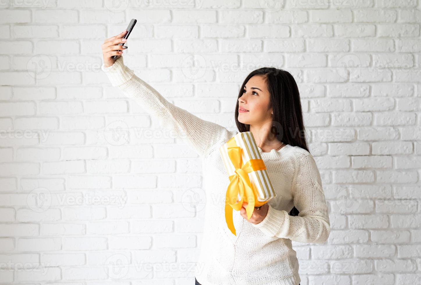 mulher segurando uma caixa de presente e tirando uma selfie foto