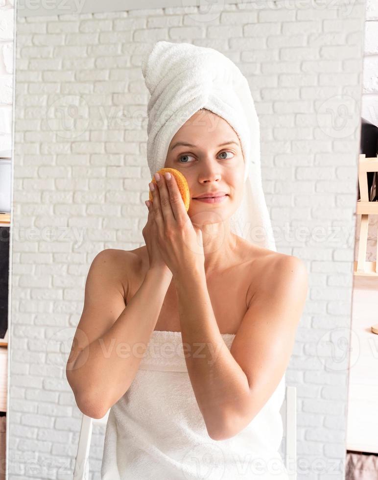 mulher com toalhas de banho brancas fazendo maquiagem matinal olhando para o espelho foto