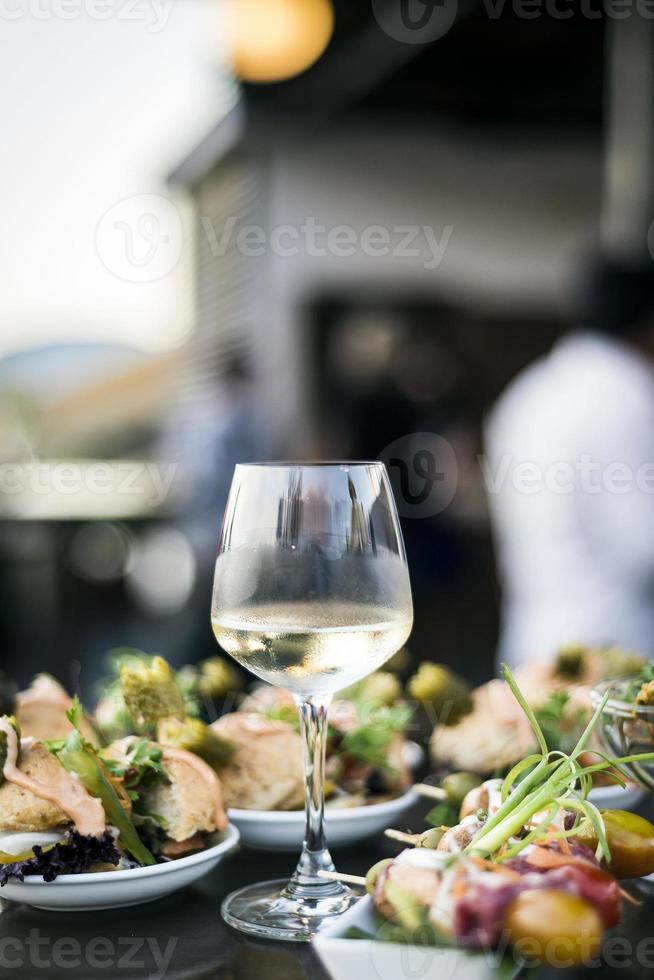 taça de vinho branco com petiscos gourmet de tapa em bar ao ar livre ao pôr do sol foto