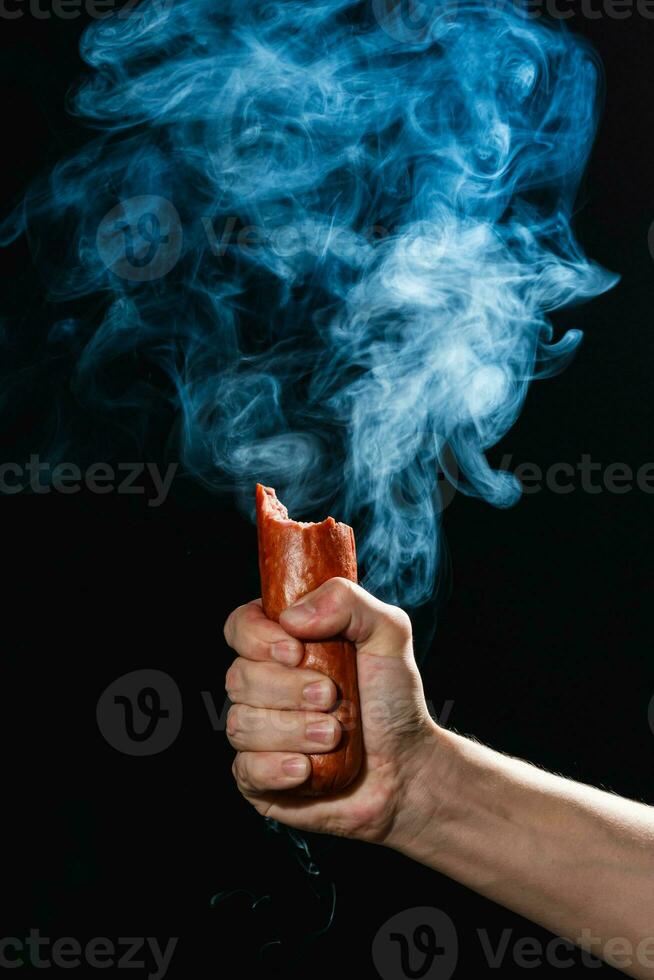 masculino mão segurando mordido defumado salame salsicha, Preto fundo foto