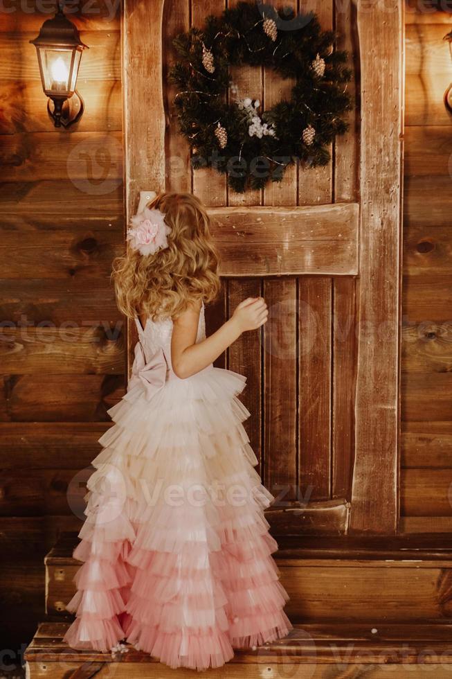 menina de vestido rosa parada na frente da porta de madeira foto