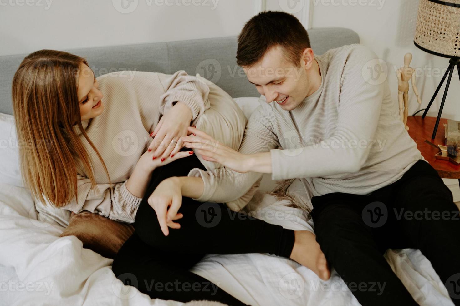 jovem casal apaixonado está deitado na cama, sorrindo e brincando foto