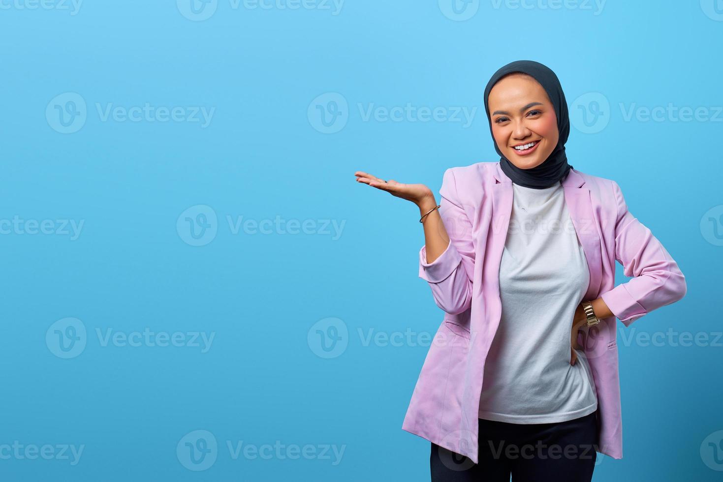 mulher asiática alegre mostrando produto sobre fundo azul foto