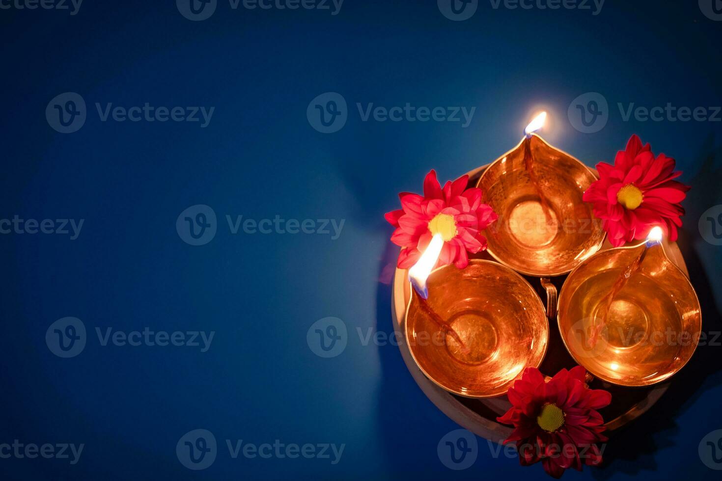 feliz Diwali. celebrando o festival indiano da luz. lâmpadas de óleo tradicionais diya e flores vermelhas sobre fundo azul foto