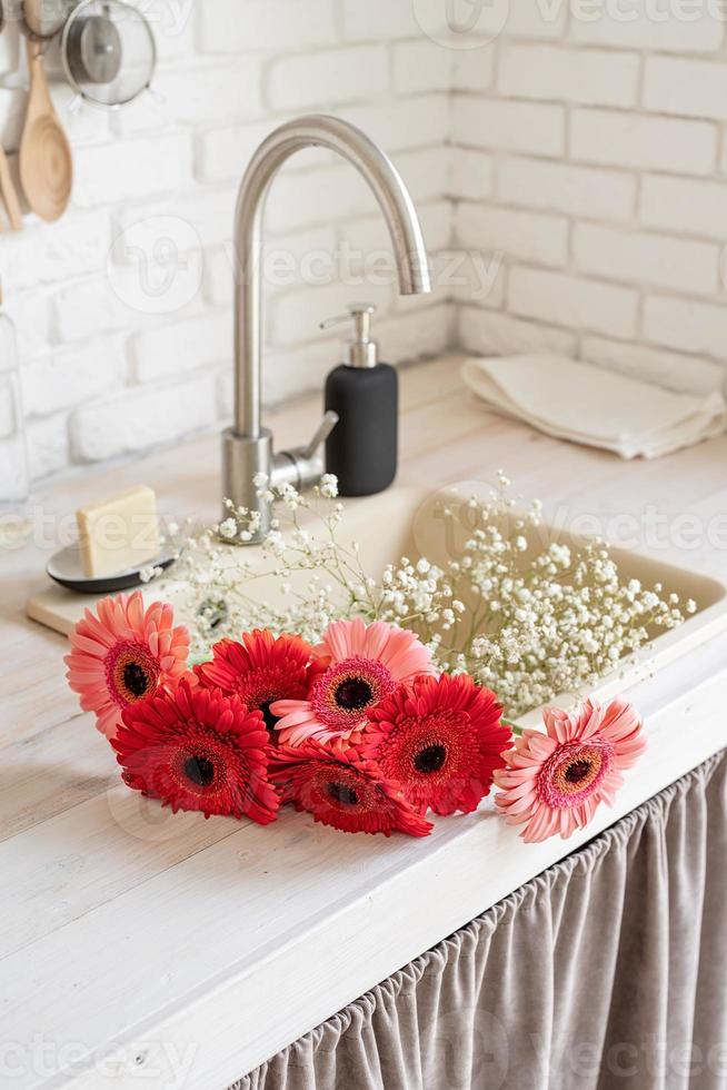 margaridas gerbera vermelha e rosa em uma pia da cozinha. cozinha rústica foto