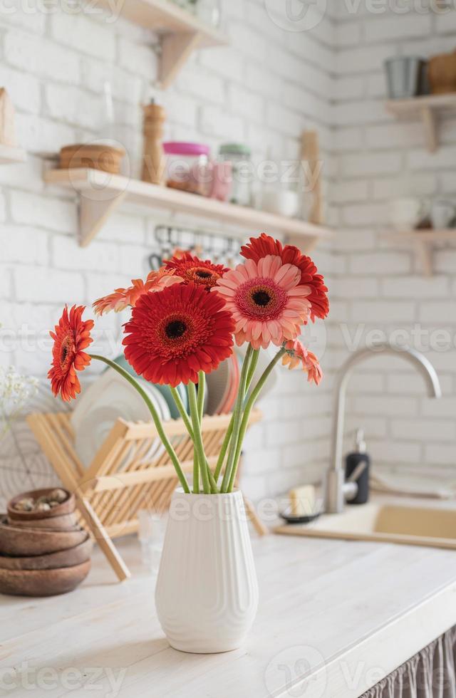 margaridas gerbera vermelha e rosa em um vaso branco em uma cozinha de madeira foto