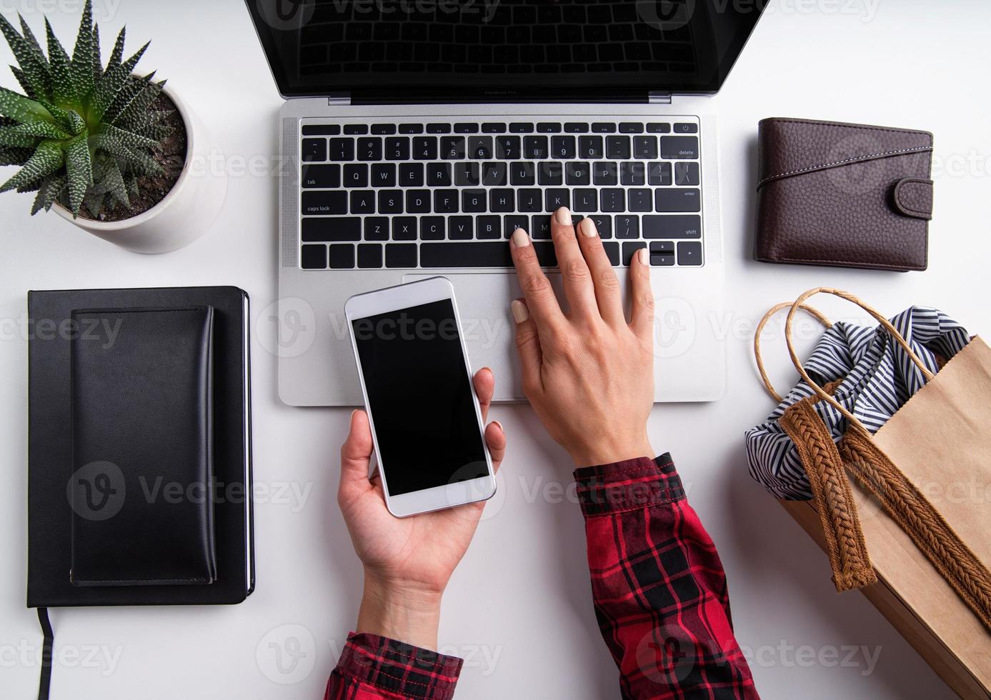 Mulher com as mãos trabalhando em um laptop segurando um telefone celular, vista superior plana leigos foto