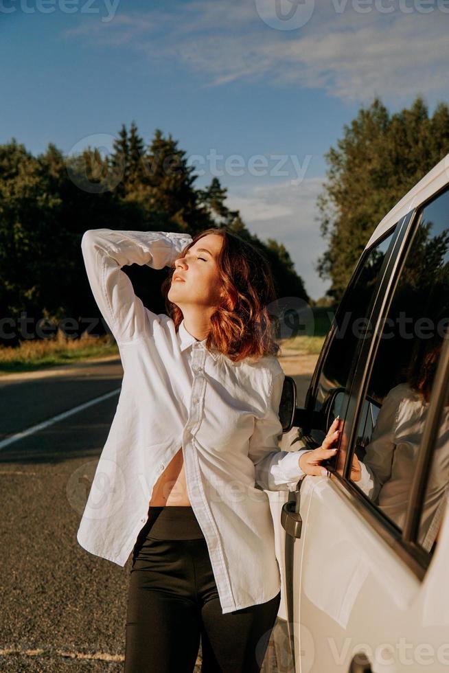 uma mulher em uma camisa branca ao lado de um carro branco na estrada foto