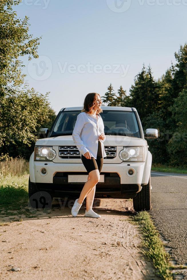 uma mulher em uma camisa branca ao lado de um carro branco na estrada foto