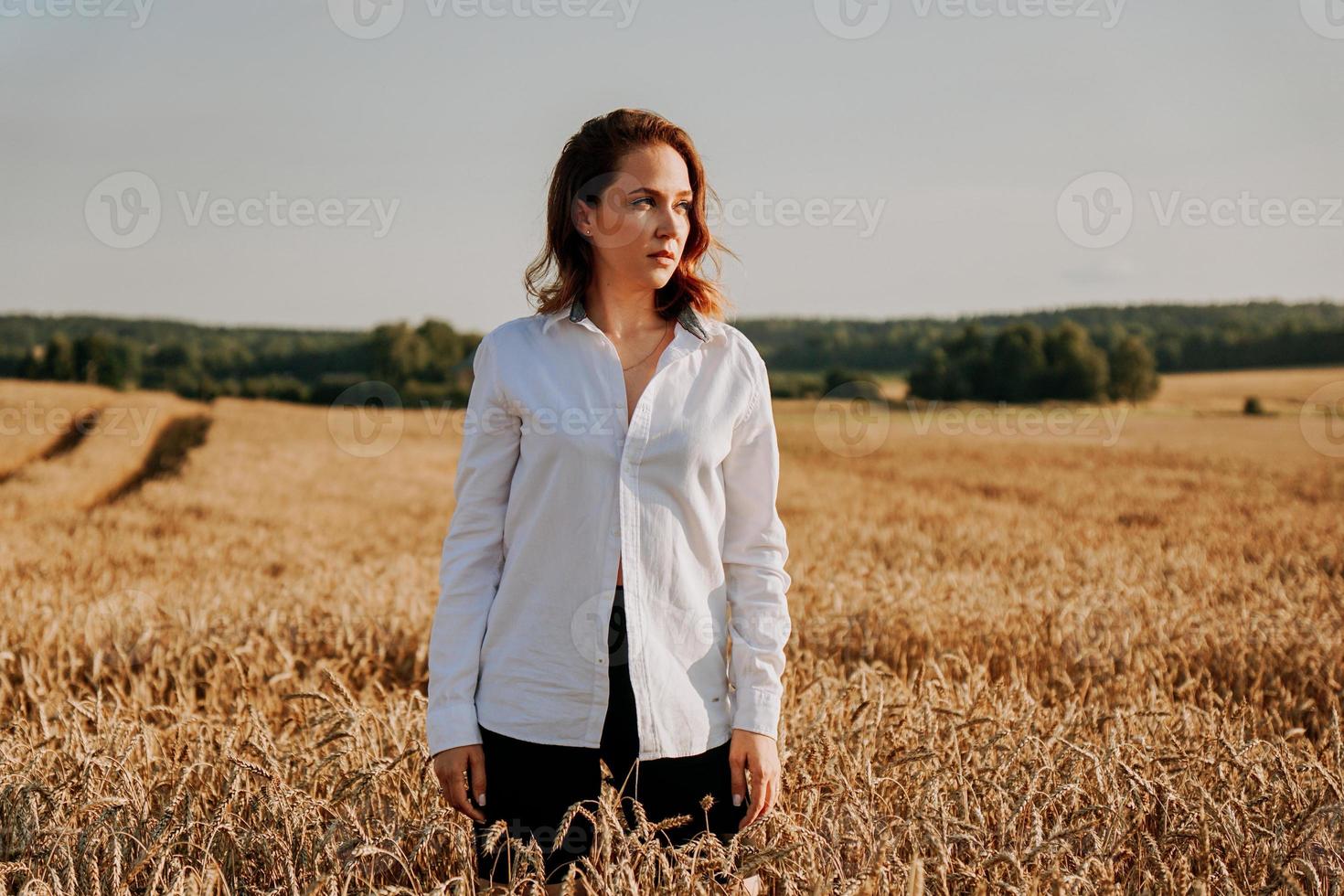 garota ruiva em uma camisa branca. ela no campo de centeio em um dia ensolarado foto