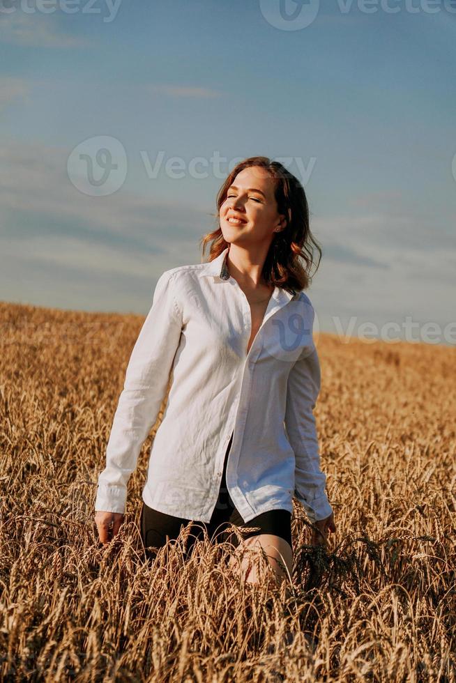 garota ruiva em uma camisa branca. ela no campo de centeio em um dia ensolarado foto