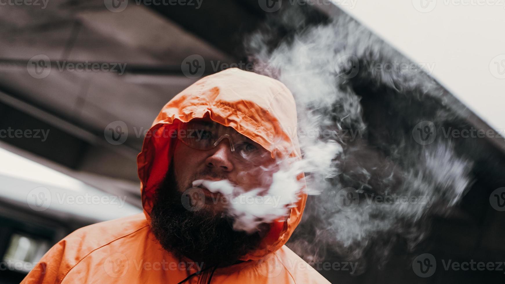 um homem de óculos de segurança e um terno laranja. homem exala fumaça foto