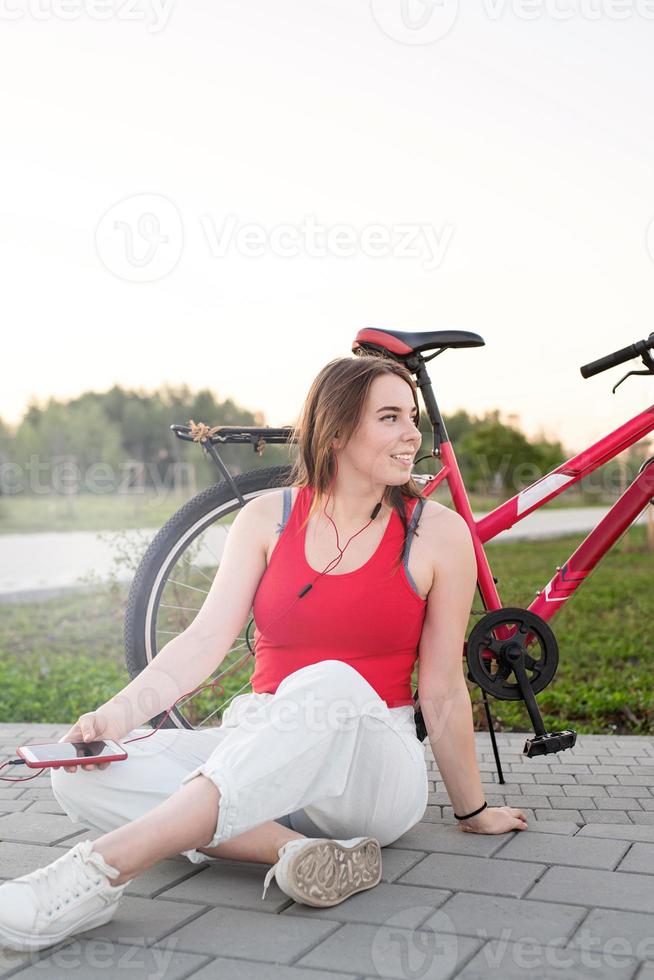 menina sentada ao lado de sua bicicleta ouvindo música no parque foto