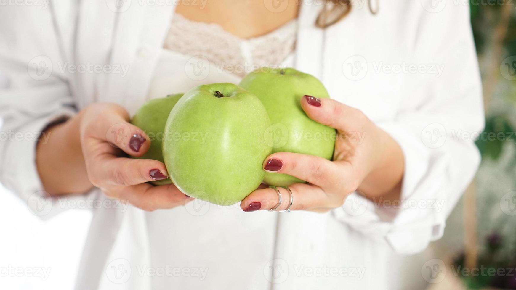 close-up de mãos femininas segurando três maçãs verdes foto