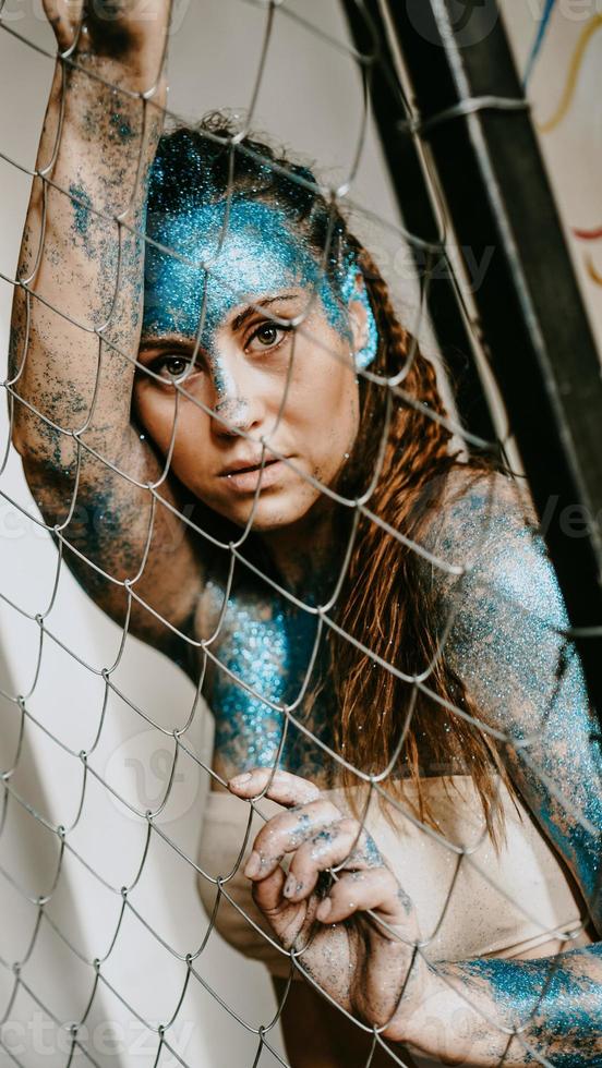 menina morena atrás da rede. mulher com brilhos azuis no rosto foto