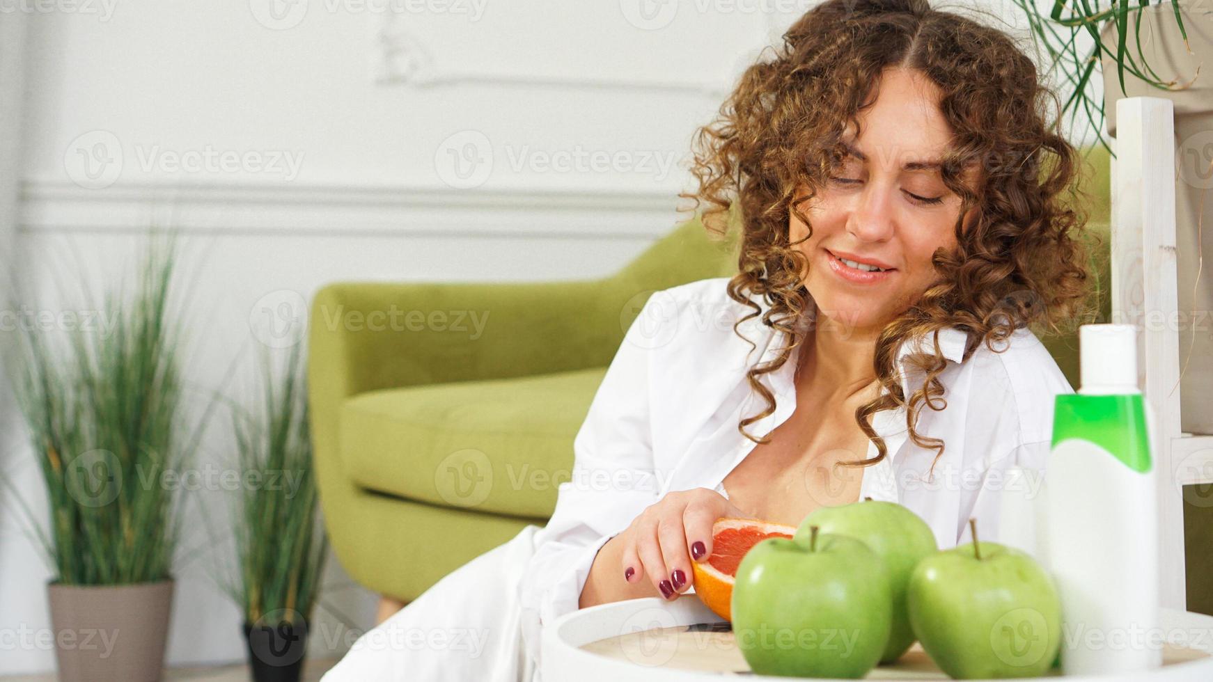 mulher com cabelo encaracolado na sala com sofá verde. maçãs e cuidados orgânicos foto