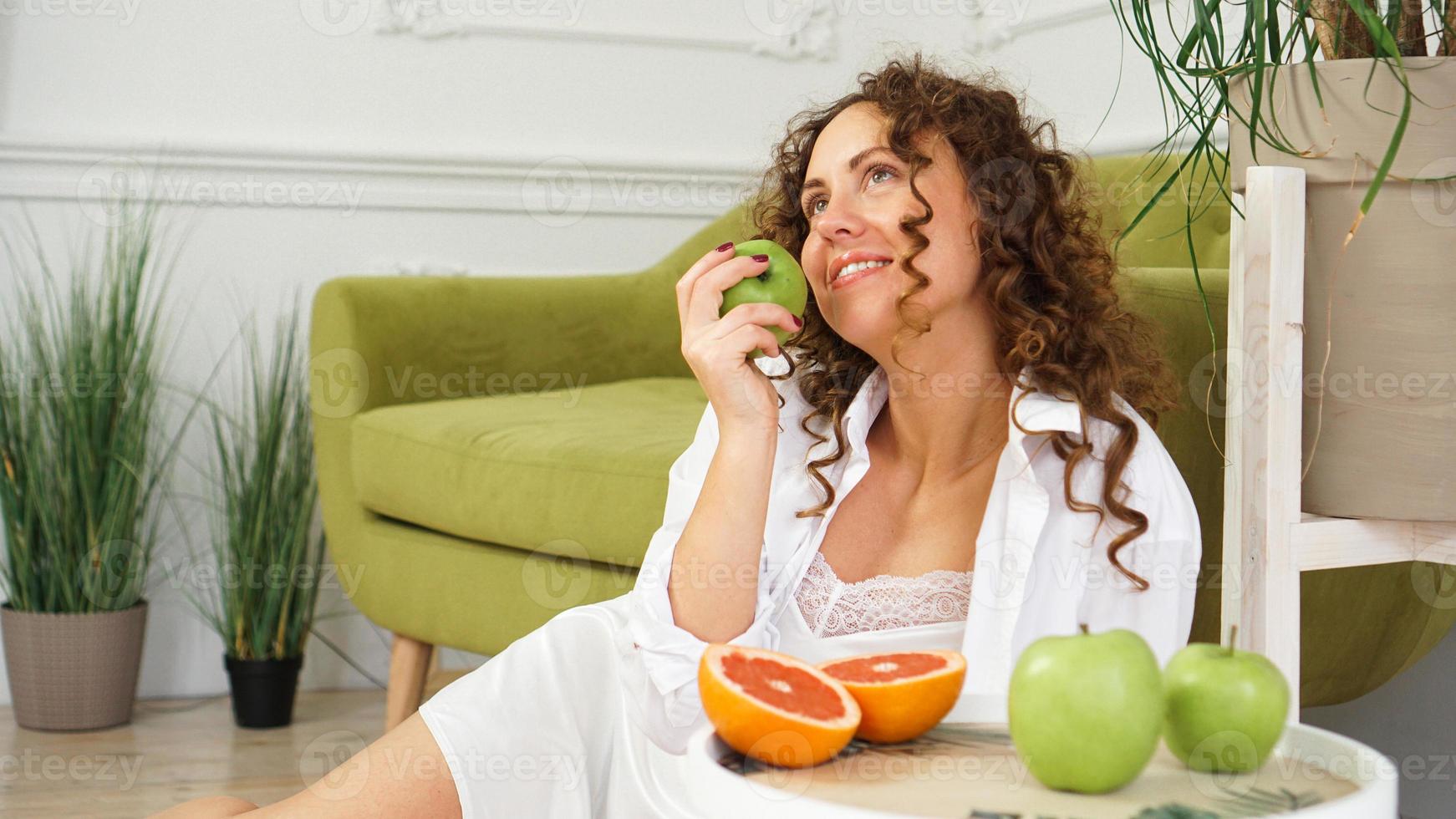 mulher comendo maçã verde em casa. nutrição saudável, conceito de dieta alimentar foto