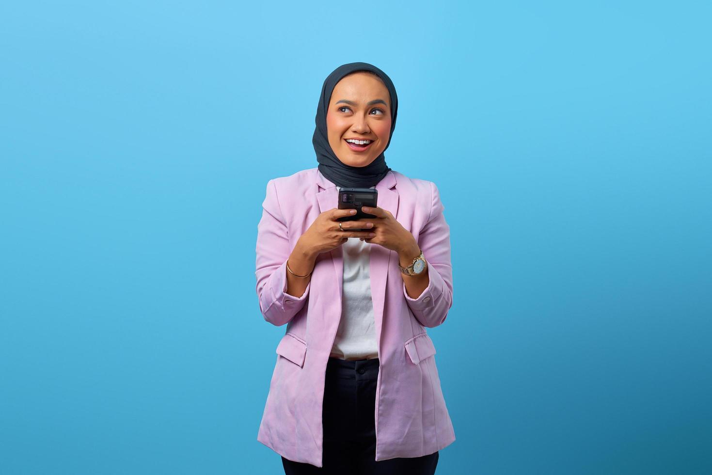 alegre mulher asiática segurando um celular e olhando para cima foto