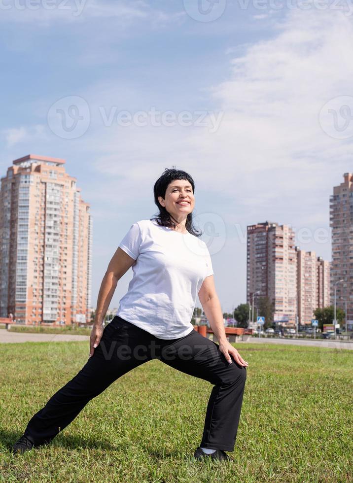 mulher idosa sorridente aquecendo alongamento ao ar livre no parque foto