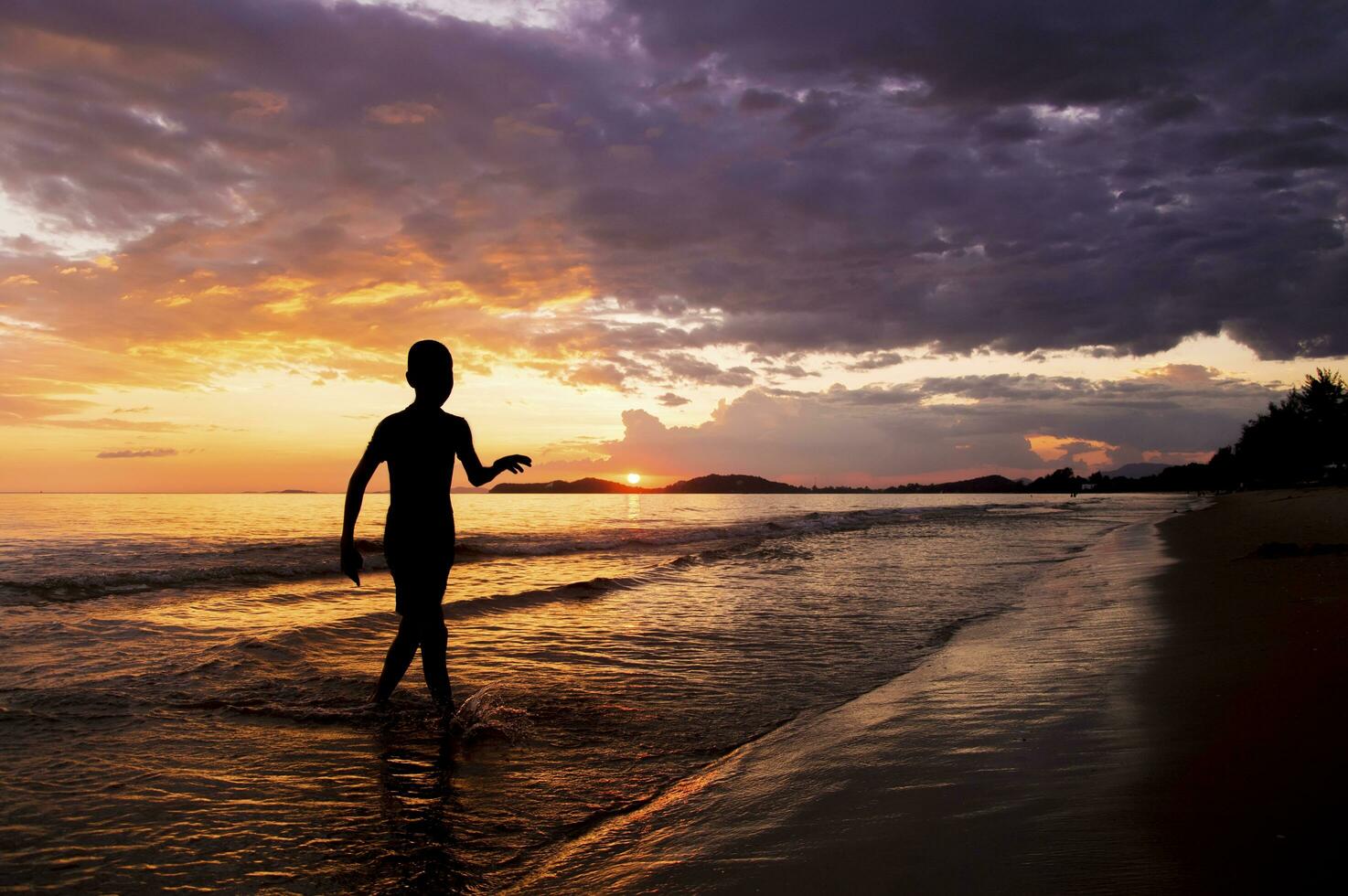 silhueta do Garoto caminhando em a de praia às pôr do sol foto