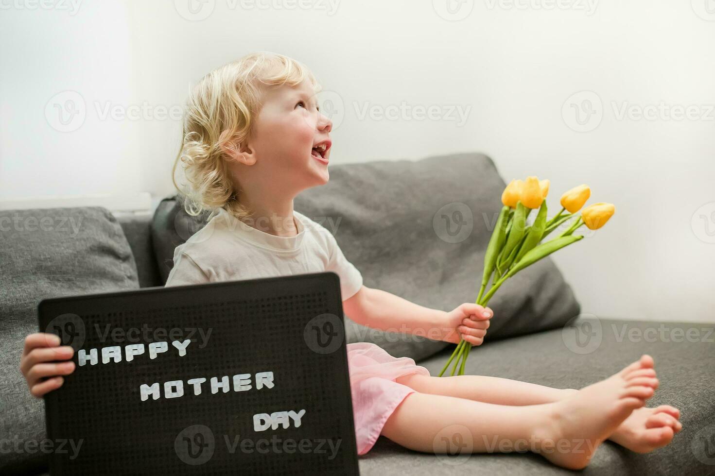 pequeno menina detém uma ramalhete do amarelo tulipas e uma placa este diz feliz mãe dia. criança dá flores para mãe para feriado. foto