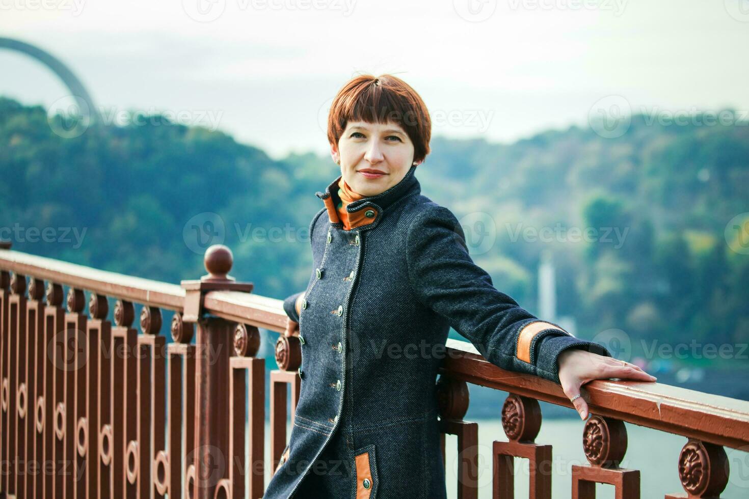 jovem mulher em pé em uma pedestre ponte dentro Kiev. a mulher com curto cabelo inclinado em a ponte corrimão. mulher em a fundo do Kiev panorama. foto