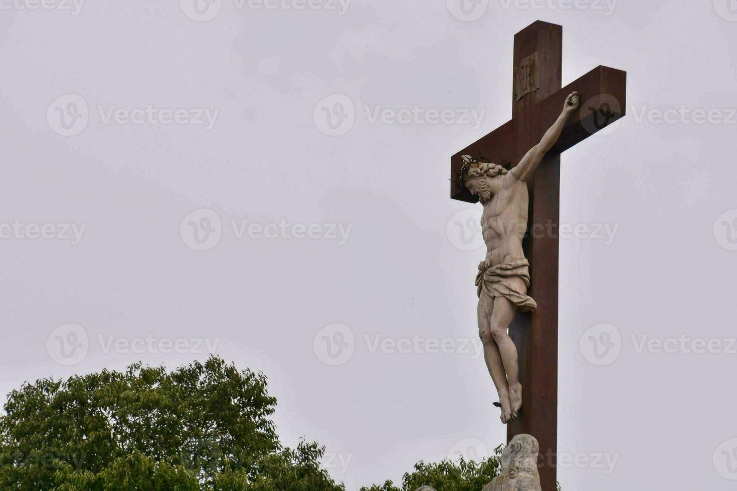 uma estátua do Jesus em uma Cruz com árvores dentro a fundo foto