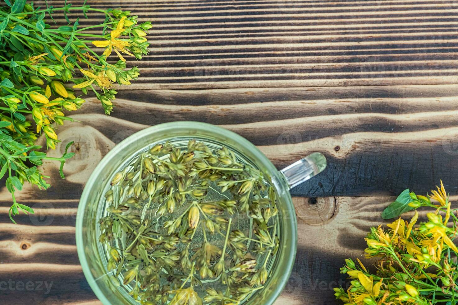 hypericum - st johns mosto plantas amarelo flor usava dentro alternativo remédio. ervas chá dentro transparente copo. útil homeopático elexir em de madeira mesa foto
