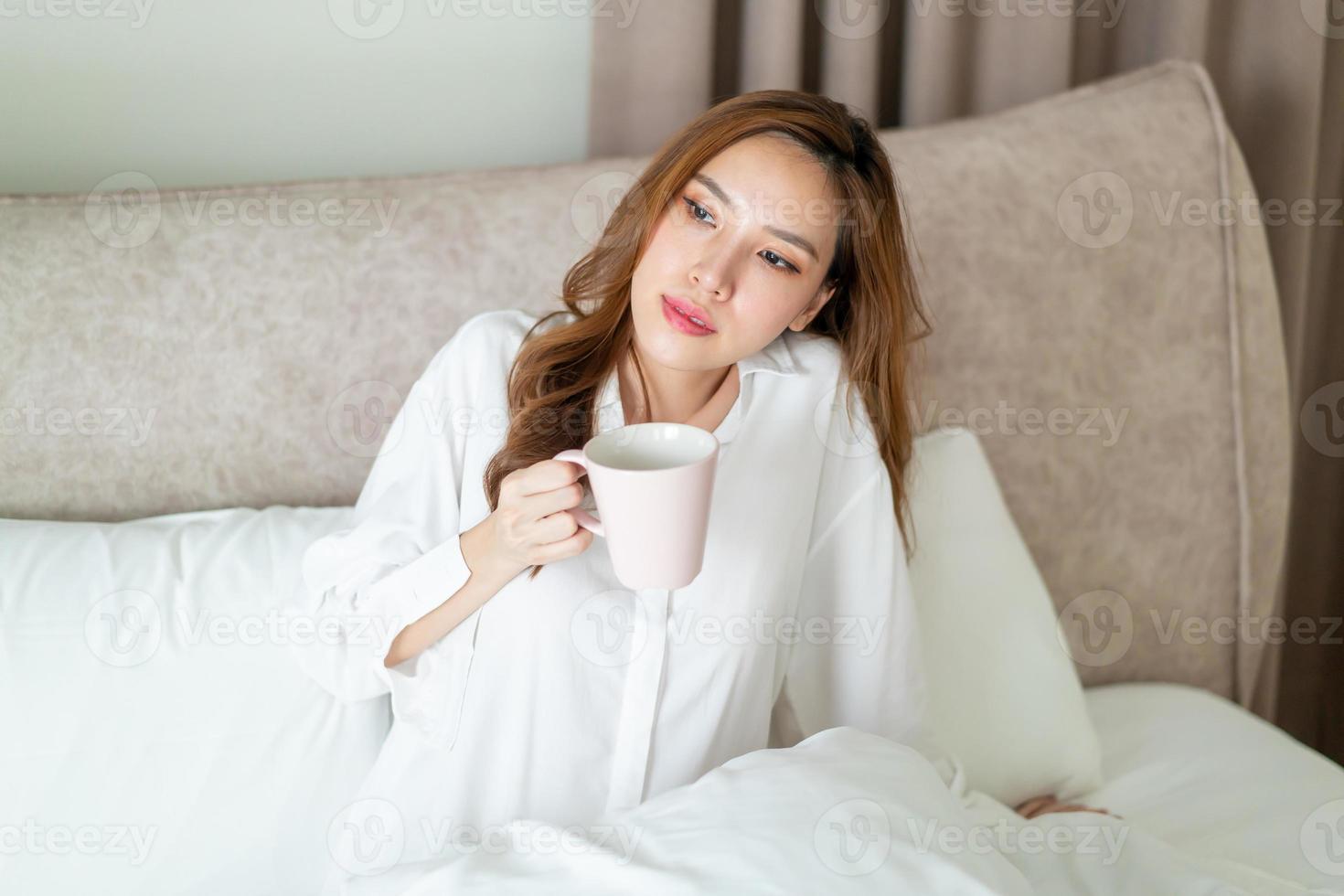 retrato de mulher bonita acordar e segurando uma xícara de café ou caneca na cama foto