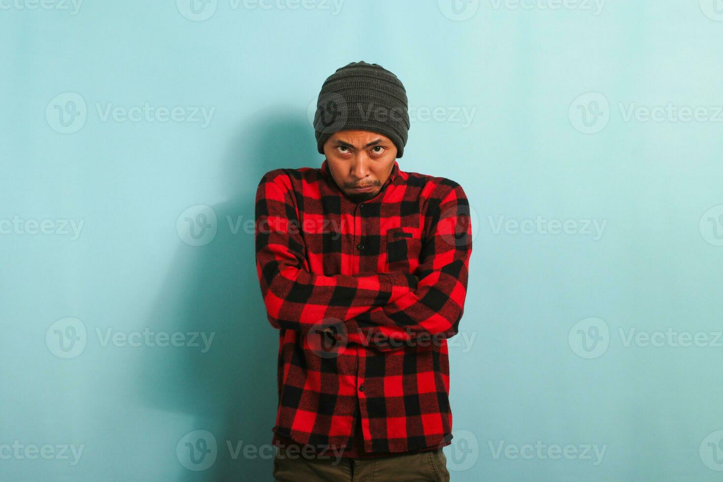 Bravo jovem ásia homem mantém dele braços guardada, esperando para explicações, isolado em azul fundo foto