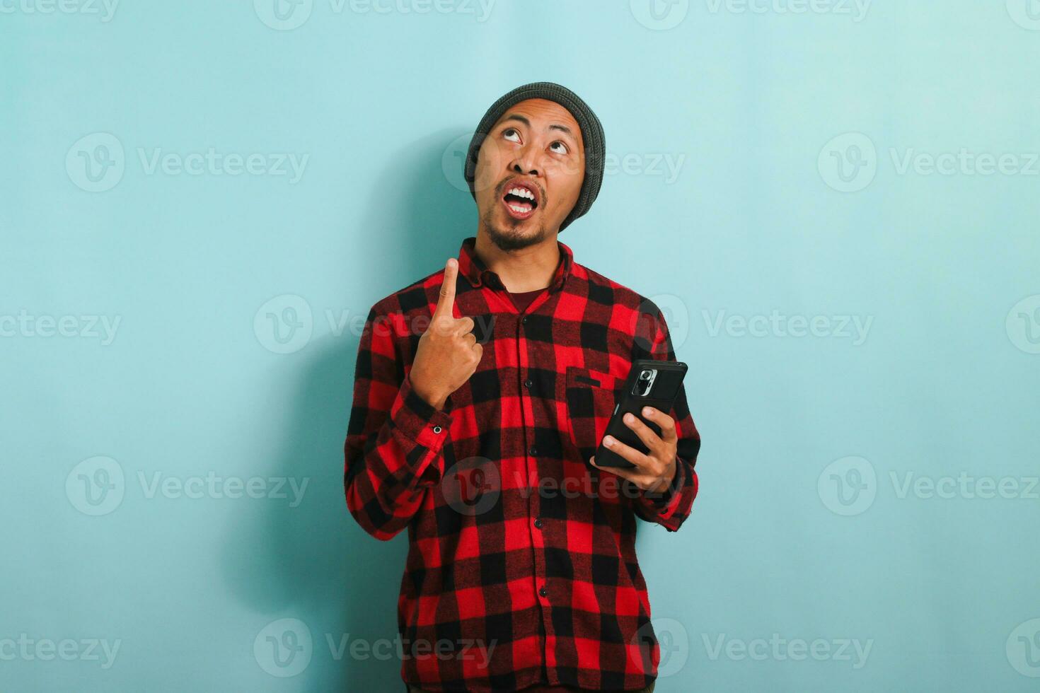 jovem ásia homem é apontando às cópia de espaço enquanto segurando uma Móvel telefone, isolado em azul fundo foto