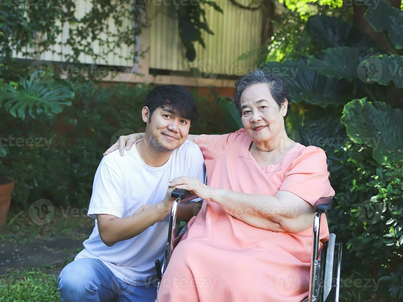 retrato do ásia Senior mulher sentado em cadeira de rodas com dela filho dentro a jardim. foto