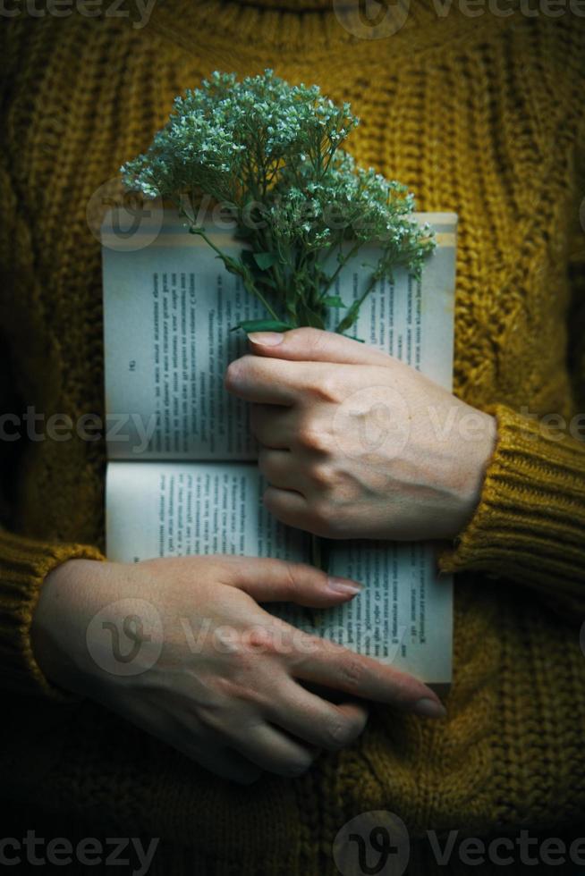 Mulher de suéter segurando um livro e um buquê foto