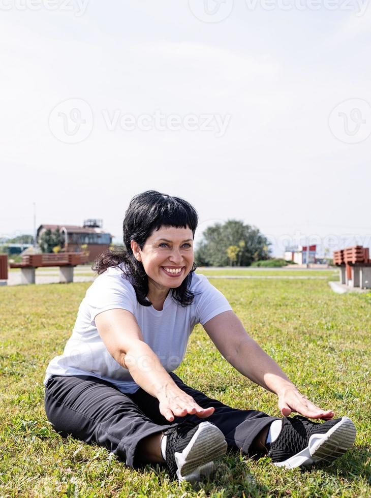 mulher aquecendo alongamento sentada na grama do parque foto