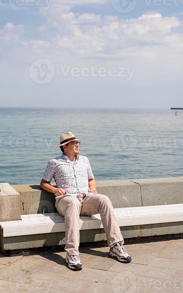 jovem sentado no banco à beira-mar foto