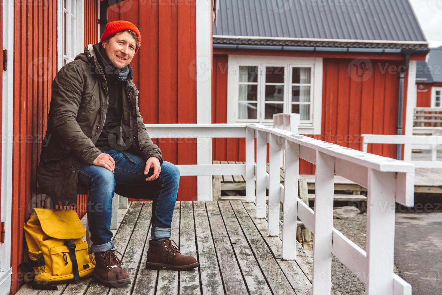 homem viajante sentado perto de casa de madeira vermelha foto