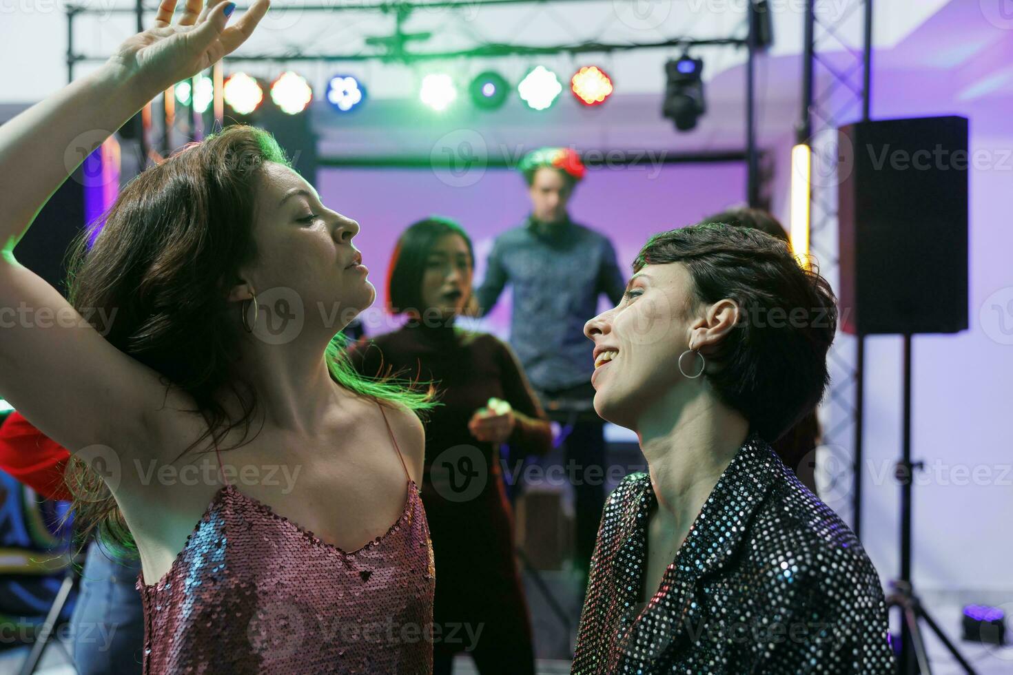 despreocupado amigas dançando e a comemorar juntos às Boate festa evento. jovem mulheres fazer enérgico movimentos em pista de dança enquanto relaxante às social encontro dentro clube foto