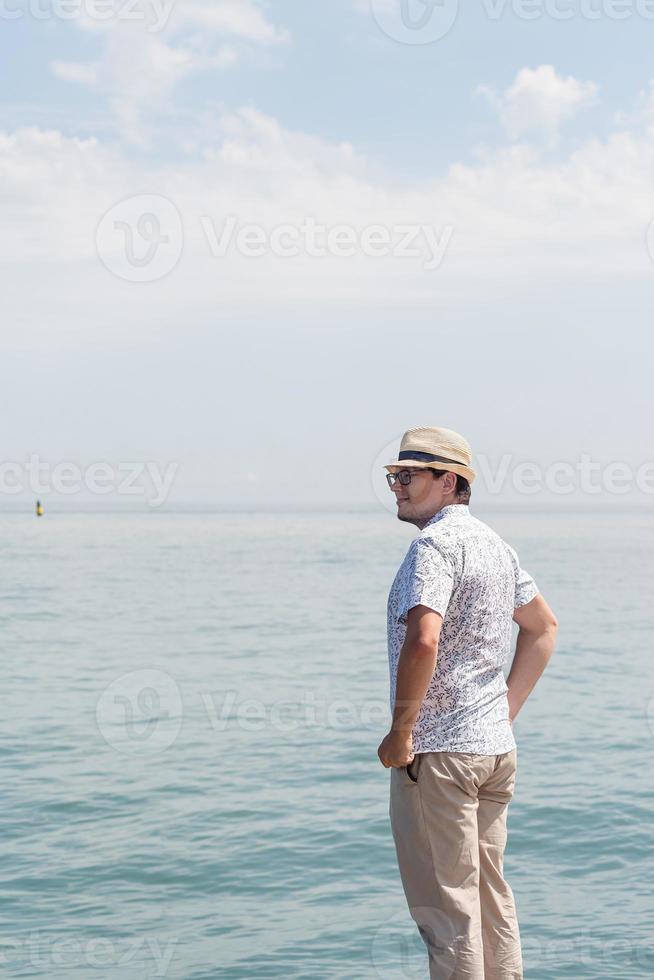 homem de chapéu em pé no cais com o mar ao fundo foto