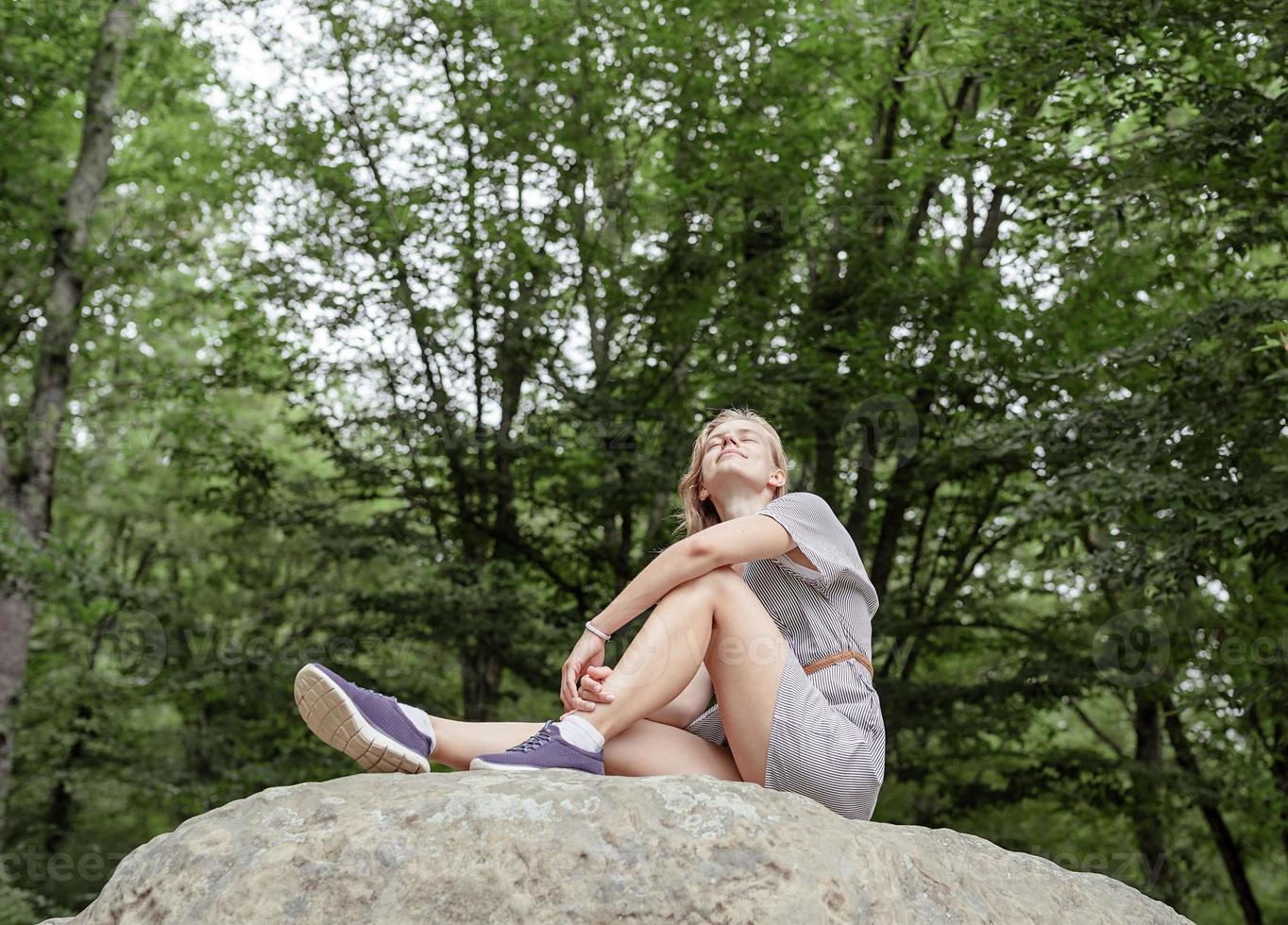 jovem sentada em uma grande pedra na floresta, olhando para longe foto