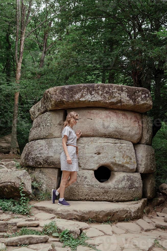 jovem caminhando perto de um grande dolmen na floresta foto