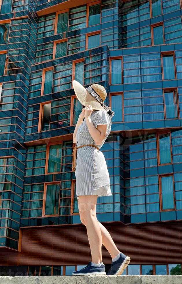 mulher com vestido de verão e chapéu em frente a um escritório moderno foto